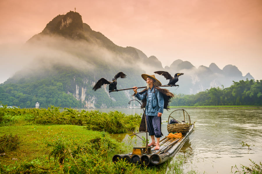 Pescador de Cormoran en el río frente a un atardecer con montañas